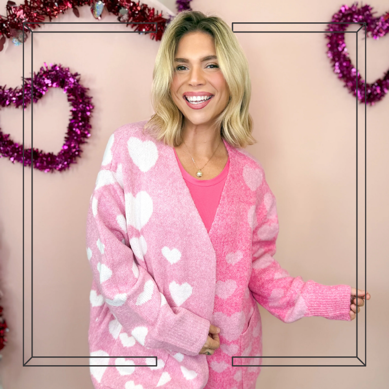 Woman wearing a pink sweater with heart patterns against a festive background | Heathered Boho Boutique | Palmetto, FL