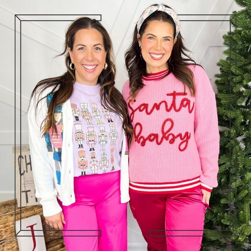 Two women wearing festive sweaters in front of a Christmas tree.